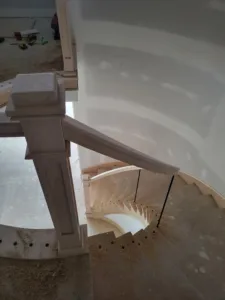 Unfinished curved staircase with a wood newel post and handrail above curved wood treads