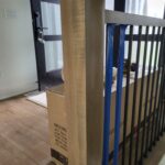 Newel post installed at stair landing with metal railing and blue balusters, raw wood finish ready for stain or paint.