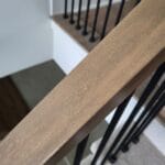 Close-up of a wooden handrail with iron balusters, showcasing the craftsmanship and finish details during the installation process.