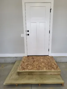 Painted white three-panel exterior door with deadbolt and knob hardware, above an OSB step landing.