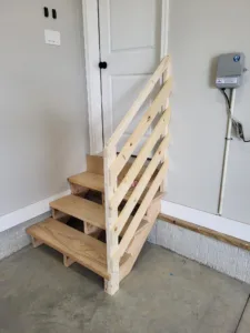 Garage stair with three open treads up to a house door, slat rail on the open side and the wall on the other