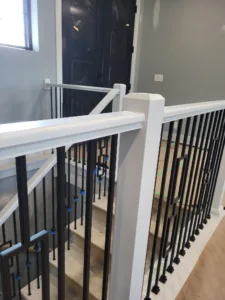 Modern staircase landing with white rail posts, horizontal black metal rod balusters, and a black door