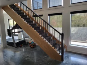 Staircase along tall window wall with wood cap rail and vertical metal balusters, carpet runner