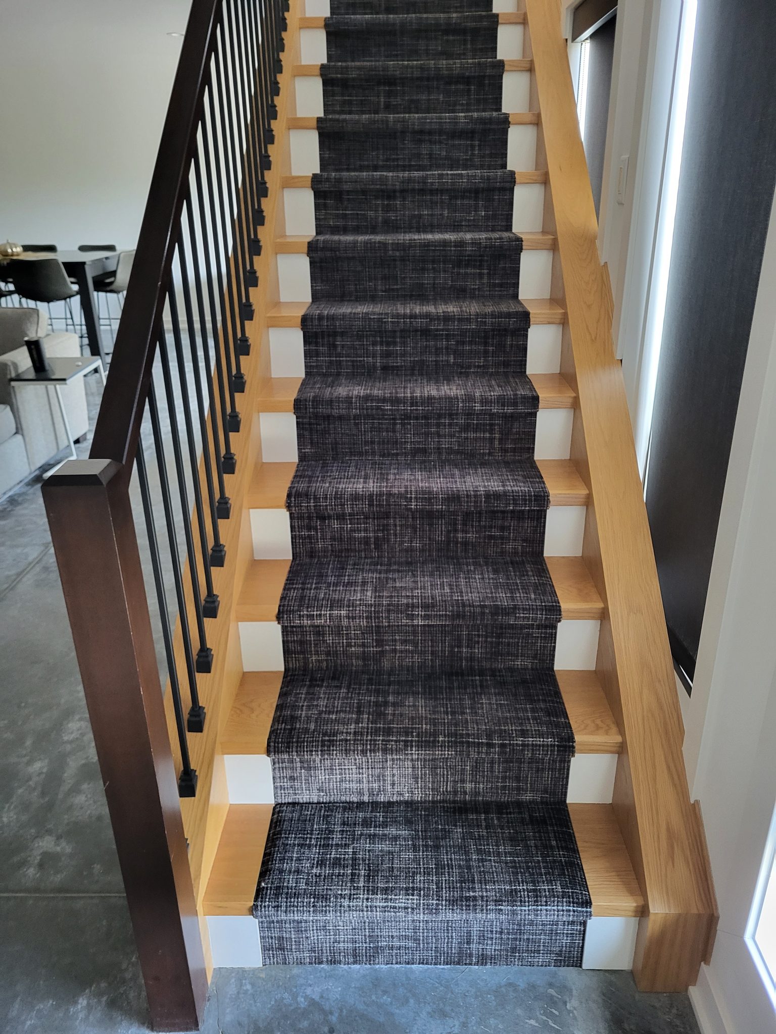 Staircase with wooden handrails and modern balusters, featuring a stylish carpet runner.
