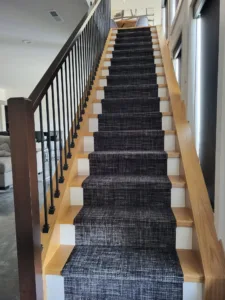 Long view down carpeted staircase with wood cap rail and vertical black metal balusters