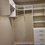 White painted face-frame closet shelving with multiple cubbies, drawers, and hanging rods installed in walk-in closet.