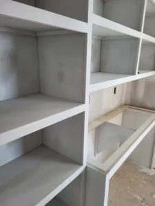 White face frame shelving under construction with open compartments, drywall dust visible, unfinished.