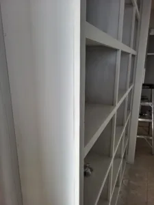 Painted white closet shelving wall with multiple compartments, construction ladder visible behind.