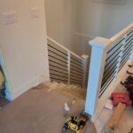 Horizontal-rod stair railing with white newel post and baseboard trim during installation.