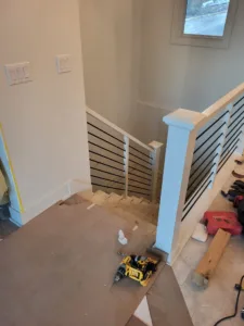 Interior stairwell during installation with horizontal metal rod railing and a newel post