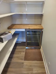Butcher block counter over white lower cabinetry and shelving, with LVP flooring in progress