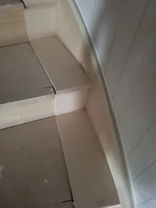Unfinished curved stair tread with a rounded end cap return against a curved wall, ready for paint