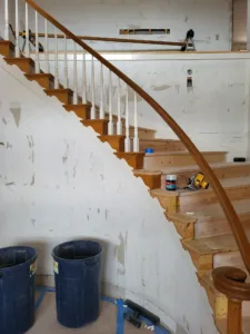 Curved staircase with painted white balusters, a wood handrail, and a notched skirt board