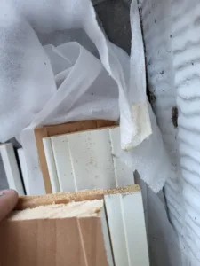 Raw wood baseboard material with primer coat, wrapped in plastic, held up to show profile edge