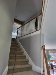 Finished staircase with black iron balusters, a wood cap rail, and carpet treads