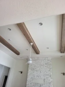 Dark stained wood beam on a flat ceiling with a fan and a stone fireplace column