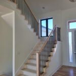 Completed stair railing with horizontal black metal rods, wood handrail, and newel posts—modern horizontal-rod style.