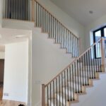Completed stair railing with horizontal black metal rods between wood newel posts and handrails.