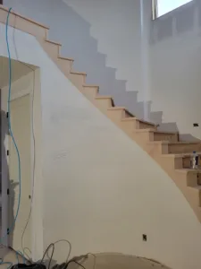 Open interior staircase in a tall foyer with raw wood treads, ready for paint or stain