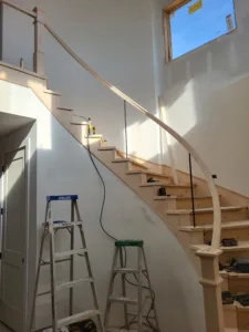 Curved staircase with treads, risers, handrail, and newel posts installed, unfinished wood ready for paint