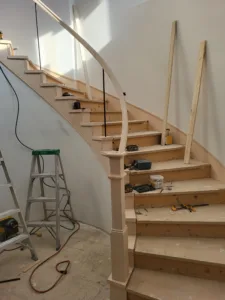 Unfinished curved staircase with a wood newel post and curved handrail during trim phase