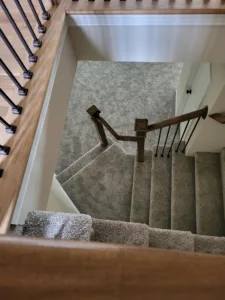 Finished staircase with a wood handrail, black iron balusters, and carpet treads