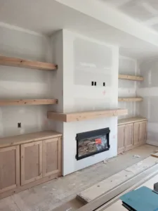 Built-in cabinetry and shelving around a fireplace, raw wood shelves and cabinet bases mid-construction