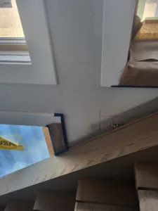 Trim corner near a window with blue painter's tape, wood stair treads below