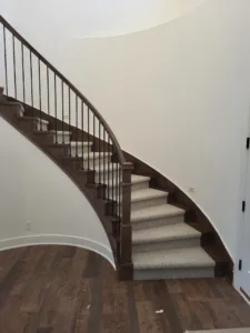 Curved staircase with dark wood skirt board, black metal balusters, and carpet-wrapped treads.