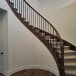 Curved staircase with dark wood skirt, metal balusters, and handrail; finished carpentry and painting complete.