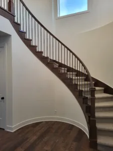 Curved interior staircase with a dark wood skirt board and black metal balusters, finished