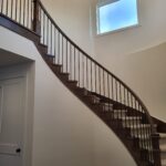 Completed curved staircase with wood skirt, metal balusters, and handrail in painted interior space.