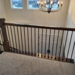 Installed newel post with handrail and metal baluster railing at stair landing, dark stain finish.
