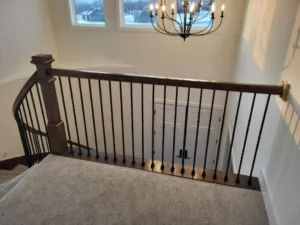 Installed newel post with handrail and metal baluster railing at stair landing, dark stain finish.