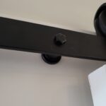 Black barn door overhead track with roller hardware mounted to ceiling.