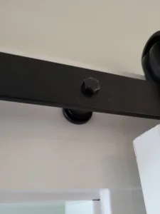 Close-up of a black overhead barn door track with roller hardware near a ceiling corner