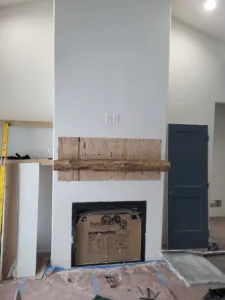 Wood mantel beam mounted above a firebox opening with plywood backing, before the shiplap surround