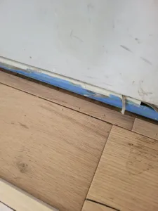 LVP flooring being installed with painter's tape protecting baseboard along the wall edge.