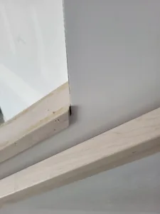 Raw wood trim piece resting against a glossy white panel, unfinished edge visible