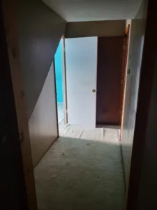 Two interior doors ajar in a narrow hallway, one painted white and one stained wood grain, jambs installed.