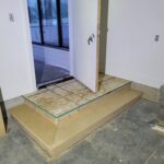 Exterior door threshold platform under construction with layered plywood base and protective tape masking.