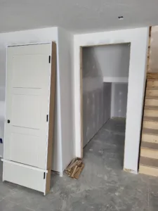 Painted three-panel door leaned against the wall beside an open cased opening leading to a stairway.