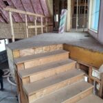 Interior stair framing in progress with raw wood treads and risers, rough construction stage.