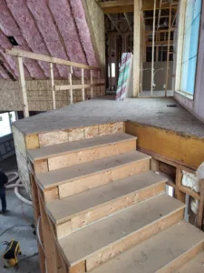 Interior stair framing stage with raw wood treads and exposed pink wall insulation