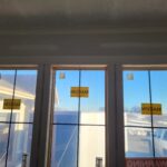 Three exterior windows with finished wood casing and protective labels, ready for paint.