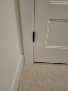 Painted six panel door with hinge visible, adjacent baseboard meets carpet flooring in hallway.