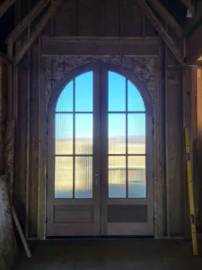 Arched double French doors with divided lites set in a rough framed opening, exterior view beyond.