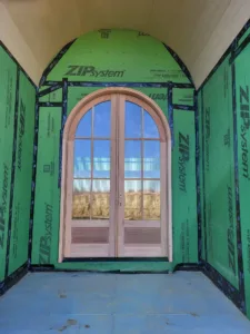 Arched glass door installed in rough framed opening with taped sheathing seams, during install
