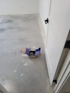Painted white door open on black hinges above bare concrete floor with construction debris nearby.