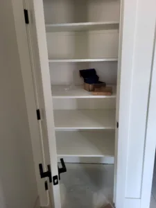 Closet shelving with five painted white shelves beside an open door showing black hinge hardware.